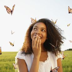 A woman holds her hand over her mouth and looks at flying monarch butterflies